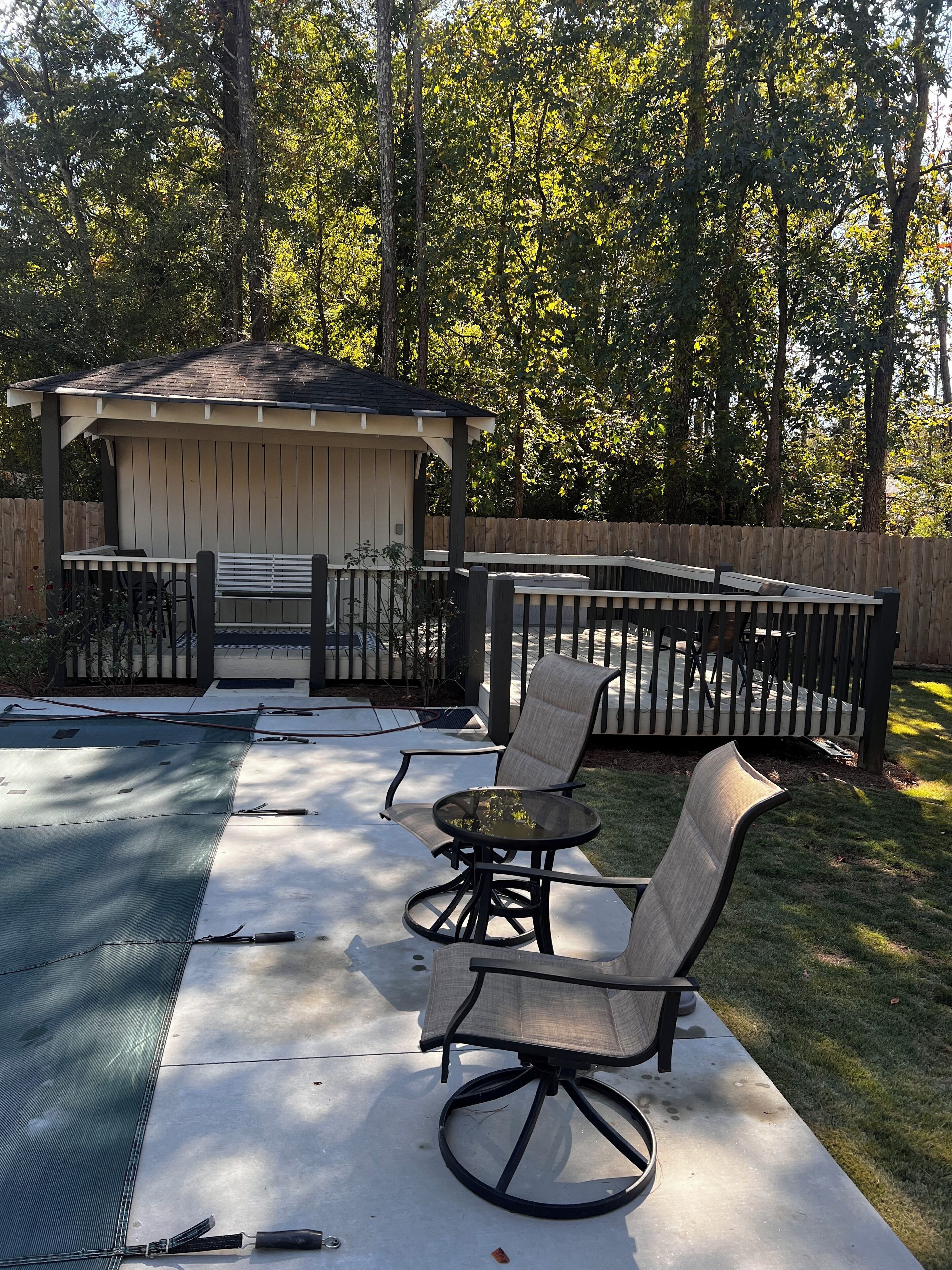 A backyard with a covered patio, a pool, and a wooden fence.