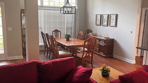 A dining area with a wooden table and chairs, a red sofa, and a chandelier. - Charming 3-bed, 2-bath house in Mableton with Wi-Fi, seasonal pool, firepit (Mableton)