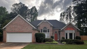 A two-story house with a brick facade, a garage, and a well-maintained lawn. - Charming 3-bed, 2-bath house in Mableton with Wi-Fi, seasonal pool, firepit (Mableton)