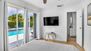Une chambre dotée d’un grand lit, d’un ventilateur de plafond, d’un téléviseur fixé au mur et offrant une vue sur une piscine.
