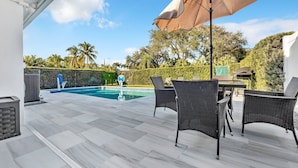 Une terrasse extérieure avec une piscine, des meubles en osier et un grand parasol.