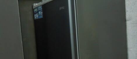 A compact refrigerator with a digital display, situated in a kitchen with a wooden floor and a green backsplash.
