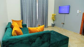 A living room with a green sofa, a flat-screen TV, and a potted plant.