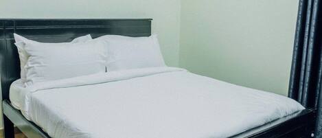 A single bed with a dark frame and white bedding in a room with light-colored wooden flooring and plain walls.