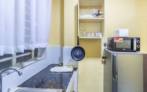 Compact kitchenette with a countertop, microwave, and hanging pan.