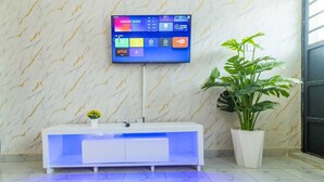 Un baño moderno con pared de mármol, tocador blanco con lavamanos iluminado en azul y una planta grande en maceta.