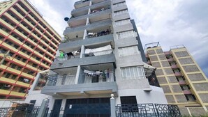 Un edificio residencial de varios pisos con balcones, entrada protegida y antena parabólica visible.
