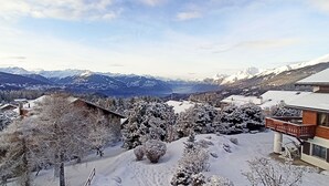 Un village de montagne enneigé, avec des maisons traditionnelles en bois et un bâtiment moderne doté d’un balcon.