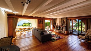 Un vaste espace de vie doté d’un plancher en bois, d’une cheminée et offrant une vue sur l’extérieur.