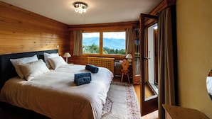 Une chambre avec un grand lit, une tête de lit en bois, une fenêtre donnant sur les montagnes et un plancher en bois.