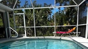 A clear blue pool with a white deck and a red and orange lounge chair.