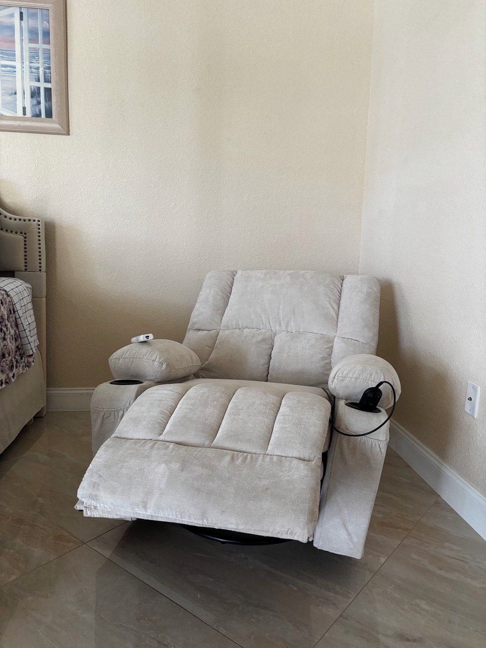 A reclining chair with a footrest, positioned against a wall with a window.