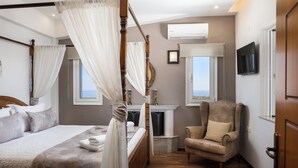 A bedroom with a four-poster bed, a fireplace, a comfortable armchair, and a television mounted on the wall.