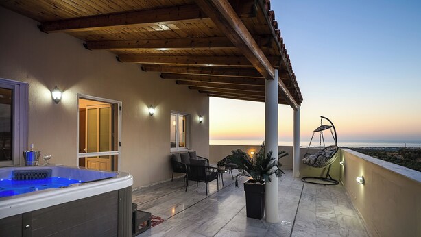 A covered outdoor area with a hot tub, seating, and a view of the sunset.