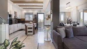 A modern kitchen with white cabinets, a dining area with a glass table, and a grey sofa.