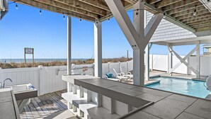Un espace piscine extérieur abrité, avec vue sur la plage, un panneau indiquant une amende en cas de violation de propriété privée, et un coin salon au bord de la piscine.
