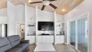 Un salon moderne doté d’un téléviseur à écran plat, de meubles blancs, d’un canapé gris et d’un ventilateur de plafond.