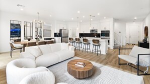 A modern living room with a white sofa, a coffee table, and a kitchen area with white cabinets and stainless steel appliances. - Gated,new 5bed home in Vegas Summerlin (Red Rock Casino area),w/ Hot Tub,BBQ,etc (Las Vegas)