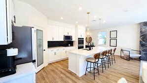 A modern kitchen with white cabinetry, a central island with bar stools, a microwave, and a stove. - Gated,new 5bed home in Vegas Summerlin (Red Rock Casino area),w/ Hot Tub,BBQ,etc (Las Vegas)