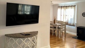 A living room with a flat-screen TV, a round console table, a dining area with a table and chairs, and a fireplace.