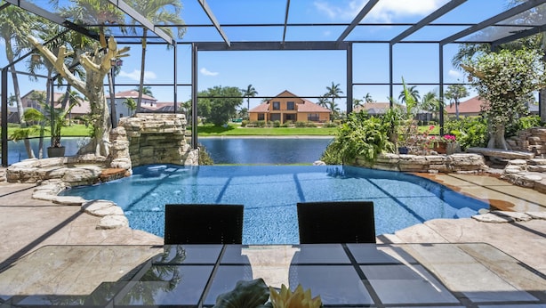 An outdoor swimming pool with stone and rock features, surrounded by a metal pergola structure.