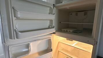 Una cocina con un microondas encima de un refrigerador blanco, que tiene varios estantes y compartimentos.