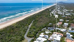 An aerial view of a coastal residential area with a beach, houses, and a road.