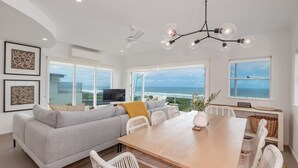 A spacious living area with a large sofa, dining table, and chairs, a TV, and artwork on the walls.