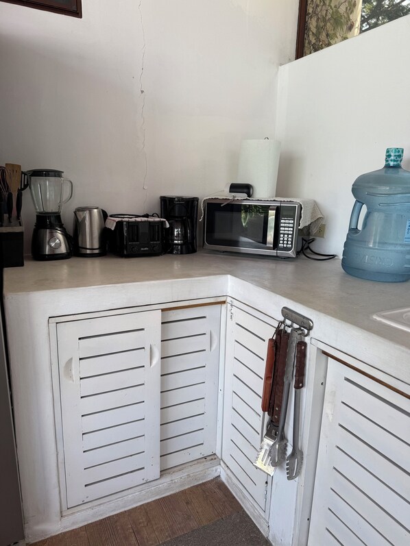 Cocina equipada con microondas, tostadora, cafetera y licuadora. Cuenta con dispensador de agua y un armario con una toalla colgando en la puerta.