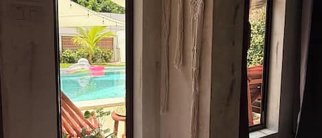 A room with large windows, a macrame wall hanging, and a round macrame stool.