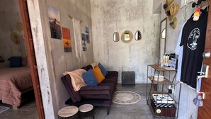 Una habitación acogedora con un sofá, dos alfombras redondas tejidas, una mesita de madera y una estantería metálica con objetos.