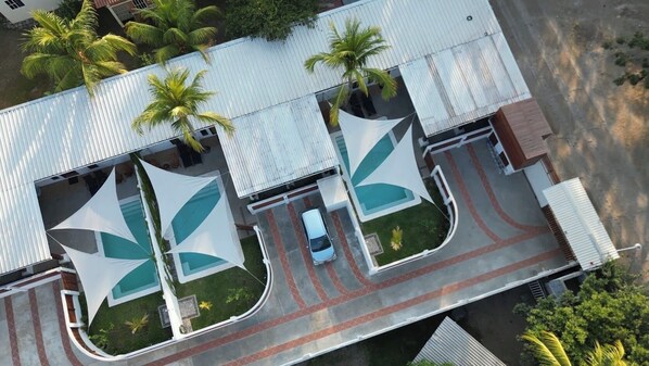 Hotel features a flat roof, triangular awnings, and a small pool surrounded by palm trees.