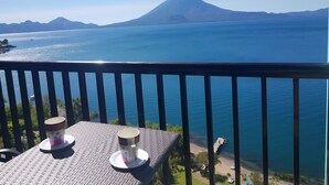 Un balcón con dos tazas en una mesa, con vistas a un lago tranquilo y una montaña a lo lejos.