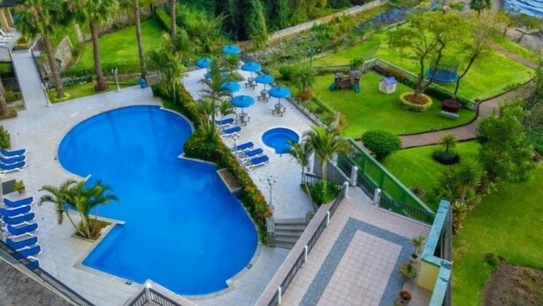 Vista aérea de un complejo turístico con una gran piscina, tumbonas y un jardín bien cuidado.