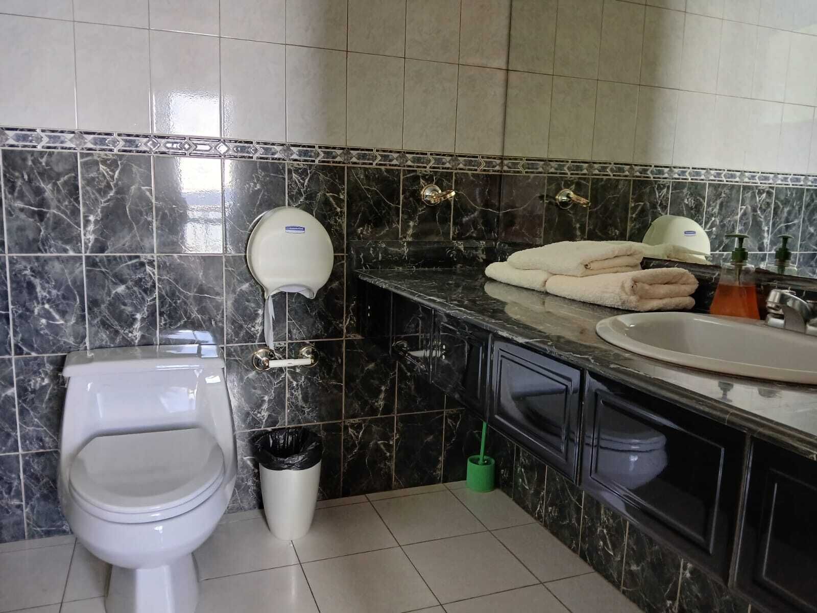 Un baño con inodoro, secador de manos, lavabo y espejo.