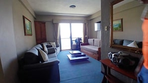 Una sala de estar con un sofá, una mesa de centro y un televisor. Hay una ventana con cortinas, una puerta y un espejo en la pared.