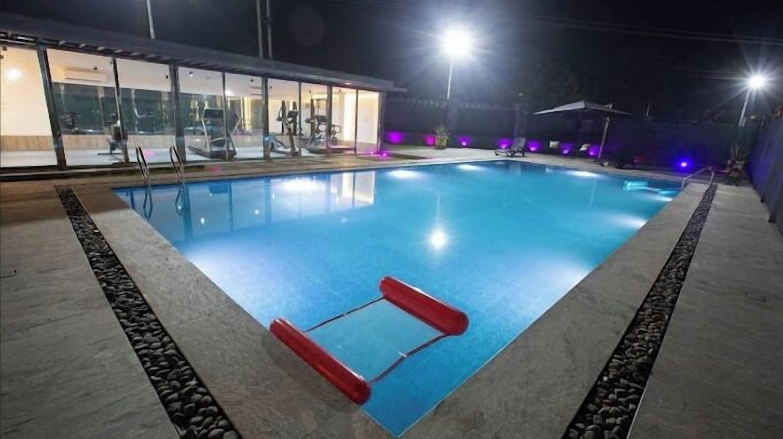 Ein Schwimmbecken mit einer roten, schwimmenden Leiter, umgeben von einer Steingrenze und einem Glasgebäude im Hintergrund.