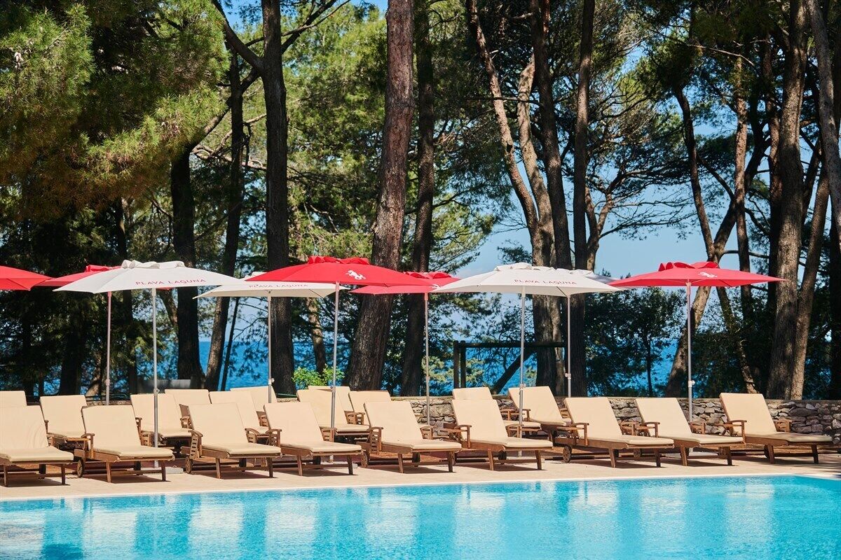 A poolside area with lounge chairs and umbrellas, surrounded by trees.