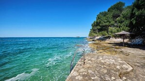 Un muelle de piedra que se adentra en aguas turquesas cristalinas, con un toldo de paja y una zona de estar a la derecha.