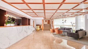 Un hall d’entrée spacieux avec un comptoir de réception en marbre, un escalier et un coin salon comprenant des canapés et une table basse.
