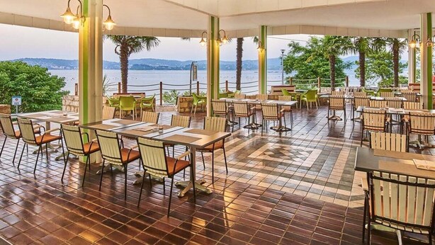 Un restaurant en plein air avec des tables et des chaises, un sol carrelé et une vue sur la mer.
