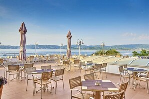 Guests can dine al fresco on the spacious outdoor terrace with tables and chairs under shaded umbrellas, offering a scenic view of the surrounding landscape.
