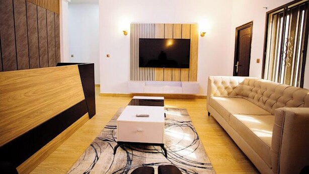 Ein modernes Wohnzimmer mit einem Flachbildfernseher, der an einer Wand aus Holzpaneelen angebracht ist, einem beigefarbenen Sofa, einer Holzbank und einem gemusterten Teppich.