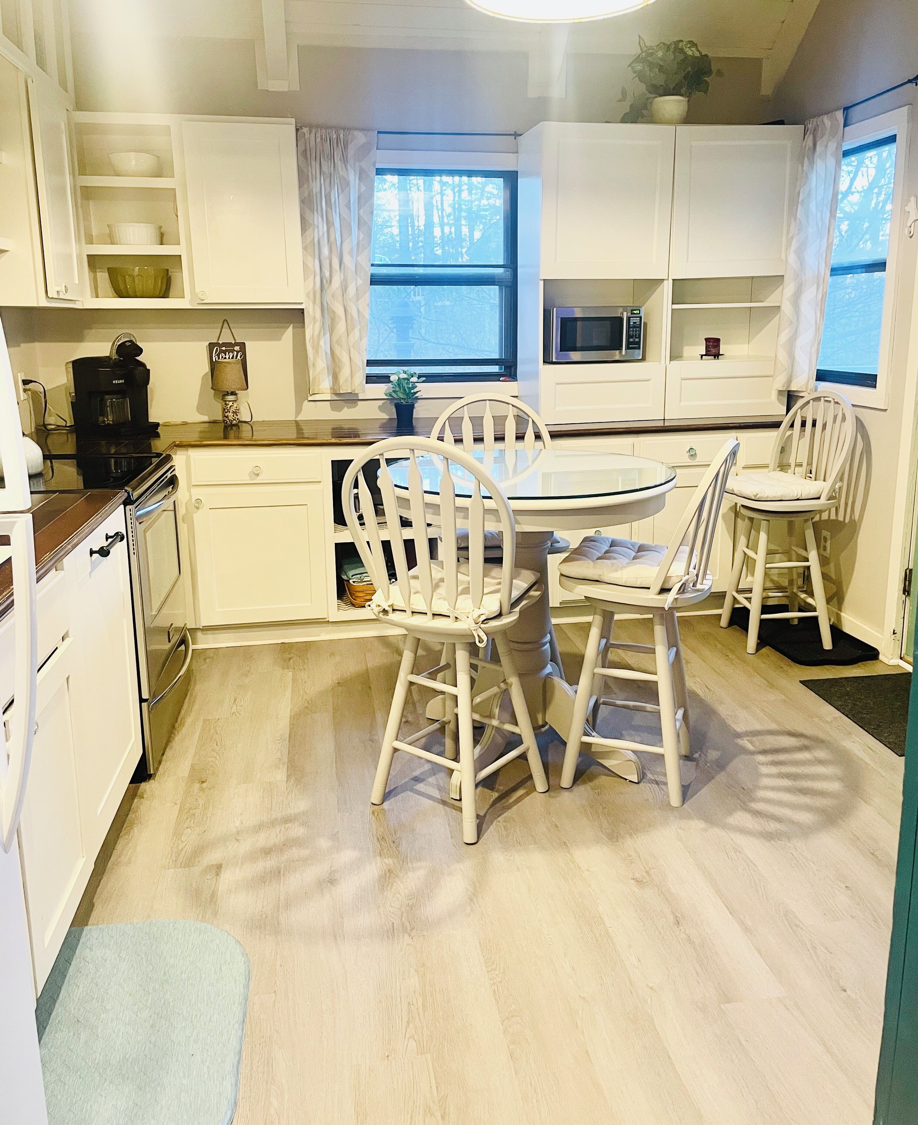 A modern kitchen with white cabinetry, a dining table with four chairs, and a coffee machine.