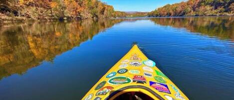 A yellow canoe with stickers on the front, floating on calm water with trees on the banks.