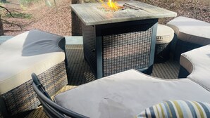 Ulkotila, jossa on neliönmuotoinen pöytä ja pehmustetut tuolit, ja jonka ympärillä on puita.