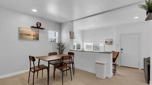 Un área de comedor moderna con una mesa y sillas de madera, un bote de basura blanco y una planta en maceta.