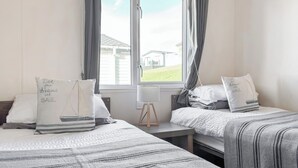 Una habitación de hotel con dos camas, una ventana con cortinas, una mesita y una lámpara.