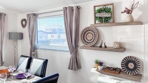 Una habitación moderna con una mesa de comedor para dos personas, una ventana con persianas, un estante en la pared con objetos decorativos y un radiador.