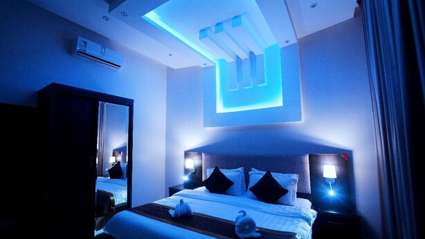 Ein modernes Hotelzimmer mit einem großen Bett, Nachttischlampen, einer Deckenleuchte und einem Spiegel.